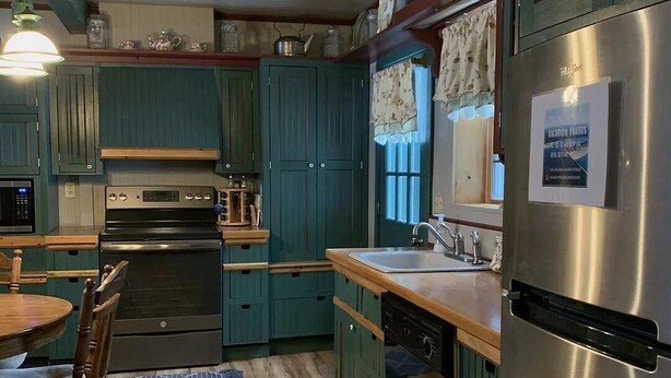 A kitchen with teal cabinets, a stainless steel refrigerator, and a wooden dining table.