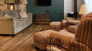 A cozy living room with a sofa, armchairs, a fireplace, a television, and a ceiling fan.