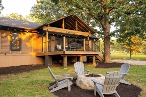 A wooden cabin with a deck, labeled '60 Ridge Lane,' featuring Adirondack chairs and a fire pit. - Resort Cabin w/ Firepit, Spacious Deck & Outdoor TV - 2 Miles to SDC (Branson)