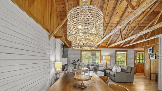 Interior de madera con una mesa de comedor, una araña y una sala de estar con un sofá y una lámpara.
