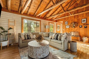 A cozy living room with a sectional sofa, a round coffee table, and wooden walls. - Resort Cabin w/ Firepit, Spacious Deck & Outdoor TV - 2 Miles to SDC (Branson)