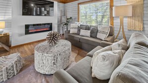 Una sala de estar acogedora con chimenea, un sofá, un otoman redondo y una lámpara colgante.