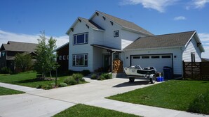 A two-story house with a garage, a driveway, and a boat parked in front. - Bozeman Basecamp - Full House - Backyard (Bozeman)