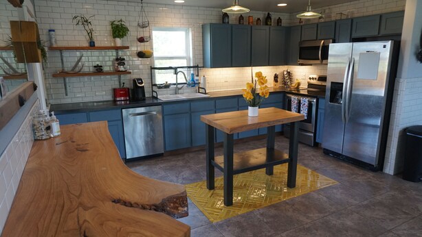 A modern kitchen with blue cabinets, a stainless steel refrigerator, and a wooden dining table with a yellow rug. - Bozeman Basecamp - Full House - Backyard (Bozeman)
