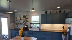 A kitchen with blue cabinets, a wooden table with a vase of flowers, and a window providing natural light. - Bozeman Basecamp - Full House - Backyard (Bozeman)