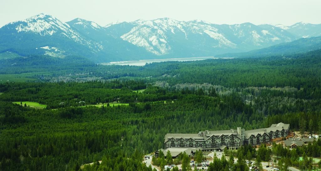 A lodge with a traditional architectural style, surrounded by dense forest and mountains in the background.