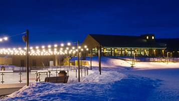 A snow-covered outdoor area with a building, benches, and a fence.