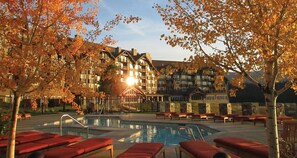 Un hotel con piscina, sillas de descanso rojas y árboles otoñales.