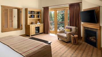 Un dormitorio con cama, televisor, chimenea, estantería y vistas al exterior.