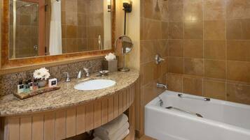 A bathroom with a granite countertop, two sinks, a large mirror, a bathtub, and a towel rack.
