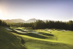 Campo de golf con búnkeres de arena, cielo despejado y montañas a lo lejos.