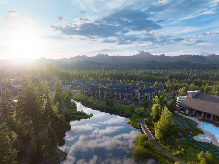 A resort with a swimming pool, a bridge, and a mountain backdrop.