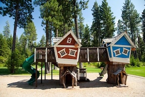 Un parque infantil con dos casitas de madera, un tobogán y un puente de madera.