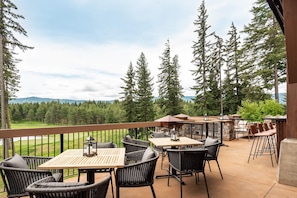 An outdoor patio with wicker furniture, a wooden table, and a view of a golf course and forest. - Suncadia Resort (Cle Elum)