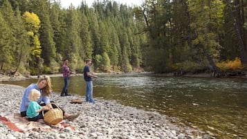 A riverbank with people sitting and standing, surrounded by trees.
