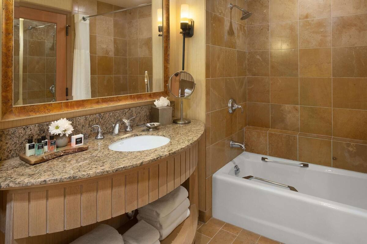 A bathroom with a granite countertop, two sinks, a large mirror, a bathtub, and a towel rack.