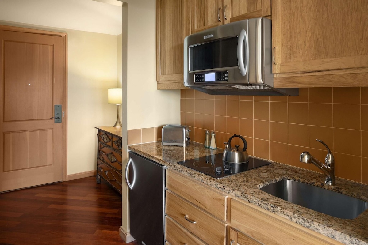 Una cocina con armarios de madera, microondas de acero inoxidable, un lavamanos y lavavajillas.