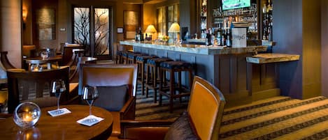 A bar area with a counter, stools, and a television screen displaying a golf game.