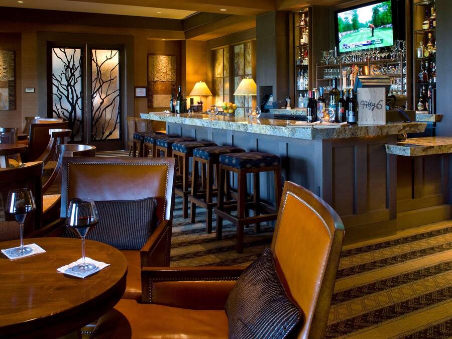 A bar area with a counter, stools, and a television screen displaying a golf game.