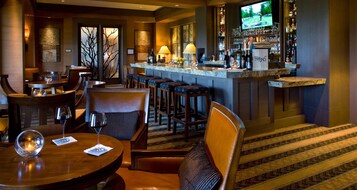 Zona de bar con barra, taburetes y una pantalla de televisión mostrando un partido de golf.