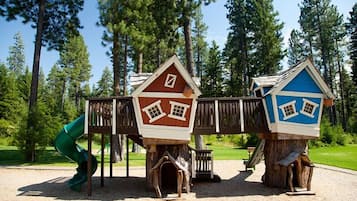 Un parque infantil con dos casitas de madera, un tobogán y un puente de madera.
