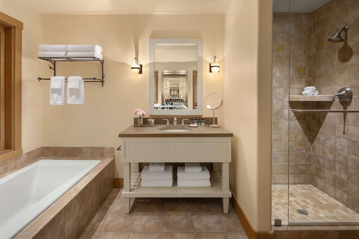 Baño con bañera, lavabo con espejo, zona de ducha y toallas en estantes.