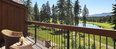 A wooden deck with wicker furniture and a view of a lake, forest, and distant mountains.