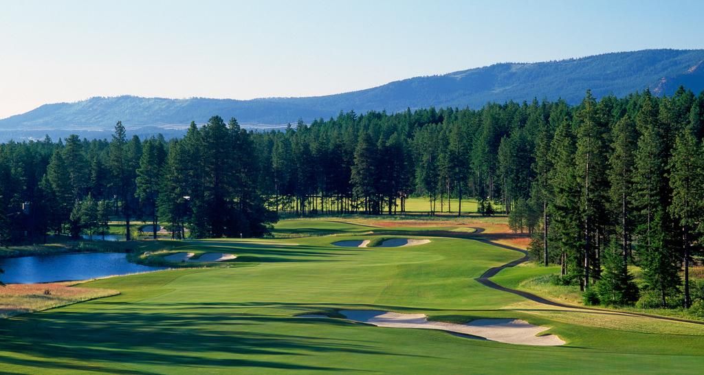 A golf course with sand bunkers, a pond, and a forested area.