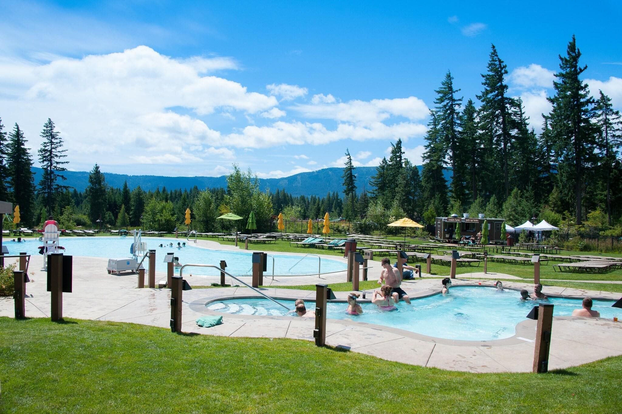 A pool area with multiple swimming pools, lounge chairs, umbrellas, and a mountainous backdrop.