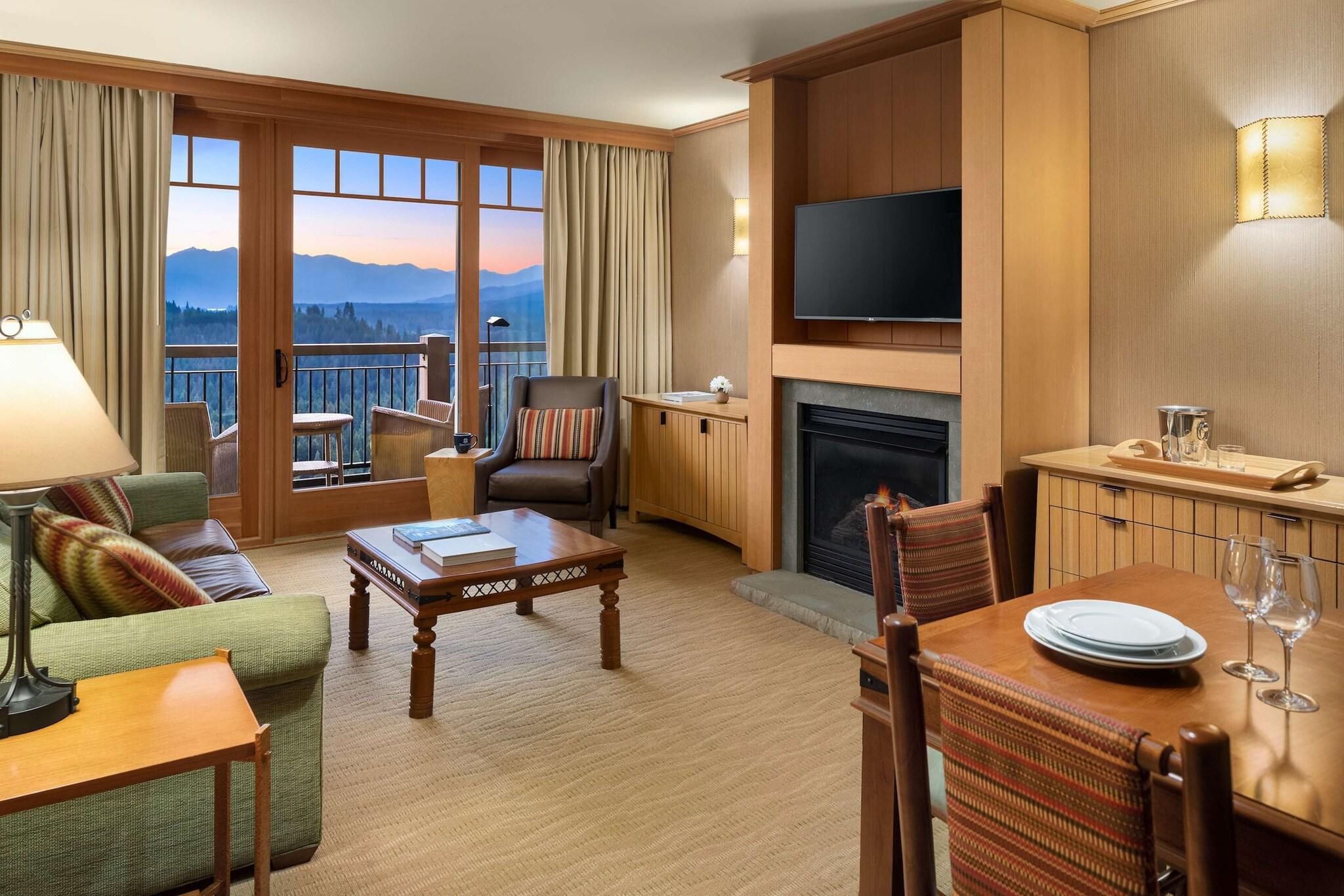 A hotel room with a balcony, a fireplace, a television, and a dining area.