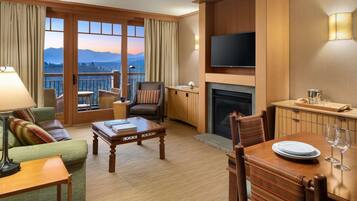 A hotel room with a balcony, a fireplace, a television, and a dining area.