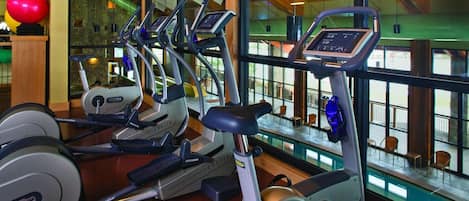 A gym with multiple treadmills, a red exercise ball, and a view of the outside through large windows.
