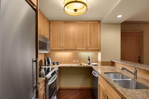 Una cocina compacta con gabinetes de madera, electrodomésticos de acero inoxidable, encimeras de granito y un microondas integrado.