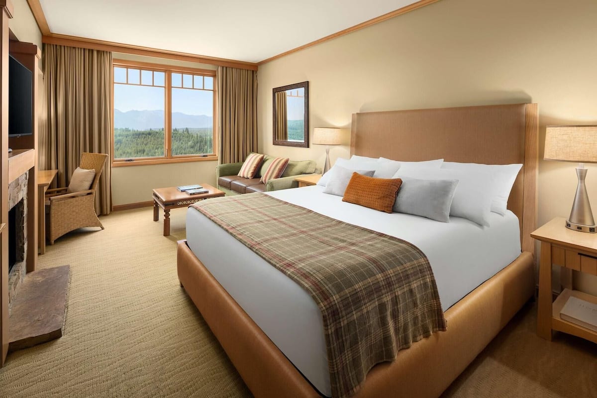 A hotel room with a large bed, a television, a sofa, a desk, and a window with a view of the mountains.