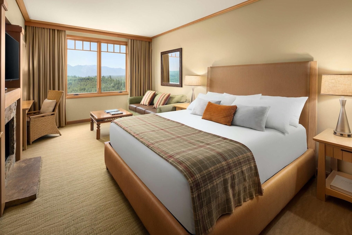 Habitación de hotel con una cama grande, televisión, sofá, escritorio y ventana con vistas a las montañas.