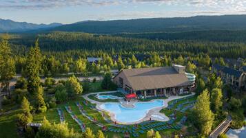 A resort with a swimming pool, a large building, and a forested area.