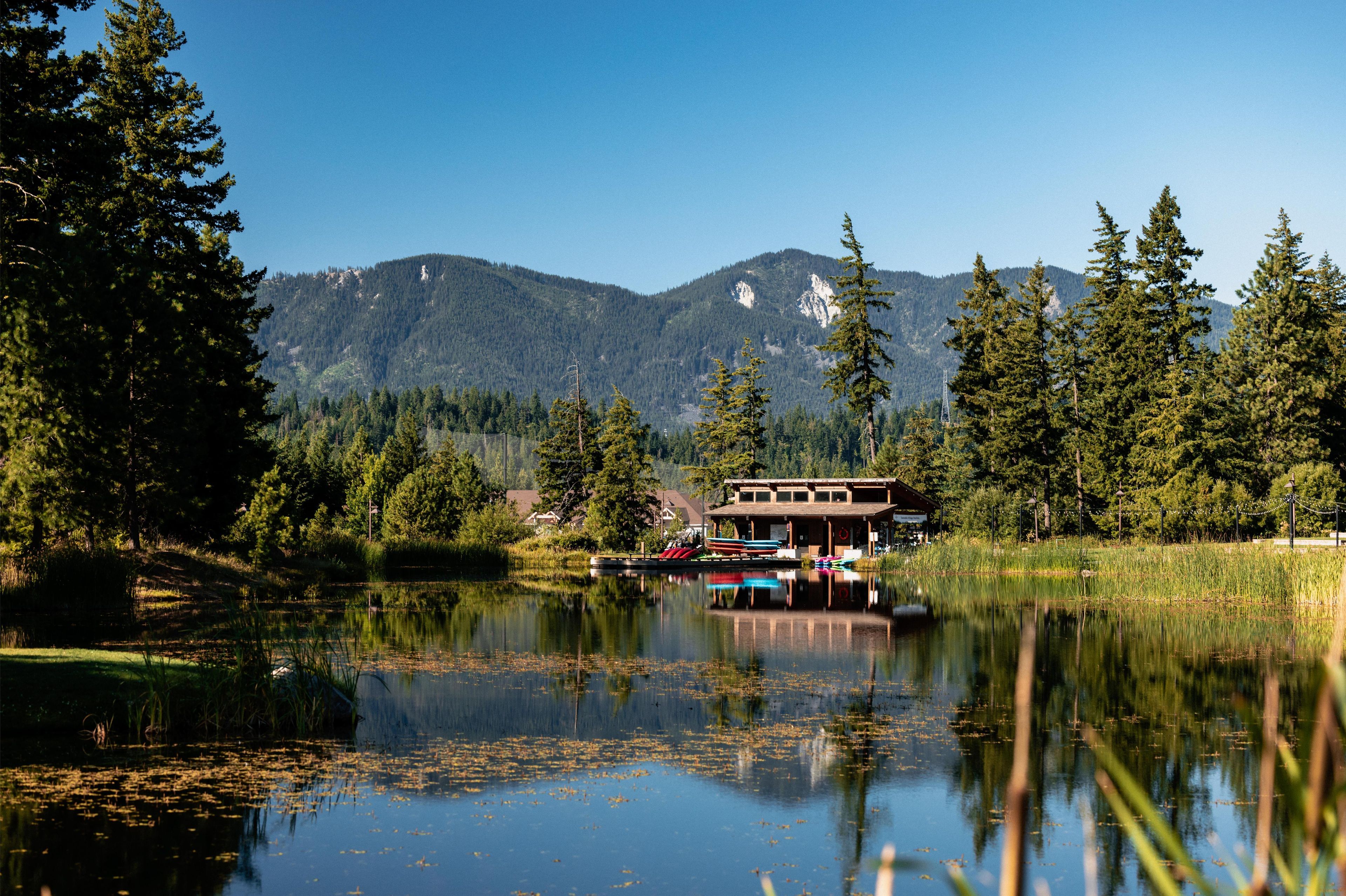 Un chalet au bord du lac, doté d’un quai, entouré de forêt et de montagnes.