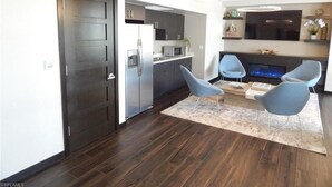 A modern kitchen with dark cabinetry, a microwave, and a refrigerator. There are two blue chairs and a small table in the living area. - Walk out the back door to #1 beaches in Naples. Renovated with new Furnishings. (Naples)