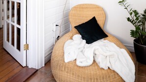 A cozy room with a wicker bean bag chair, a black pillow, and a white blanket. There's a potted plant and a patterned rug on the floor. - Steps to Main Street, Picton w Sandbanks Pass, Bbq and Large Private Back Yard (Picton)