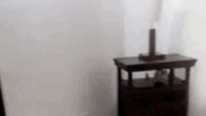 Ein Zimmer mit Fliesenboden, einem dunklen Holfnachtkästchen mit Lampe und einer weißen Wand.