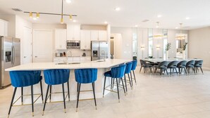 A modern kitchen with a central island, bar stools, and a dining area with chairs. - 11BR Grand Villa with Epic Game Room Near Disney (Kissimmee)