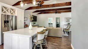 Una cocina amplia con una isla grande, vigas de madera y un refrigerador empotrado.