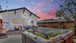 Un patio con mobiliario exterior, luces colgantes y una parrilla.