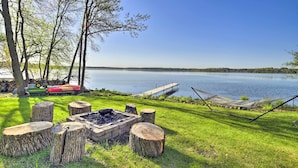 Un espace de camping au bord du lac, équipé d’un foyer, de souches en bois, d’un hamac et d’une jetée.