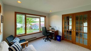 Una habitación con un ventanal grande, un escritorio con computadora, una silla y un sofá con almohadones a rayas.