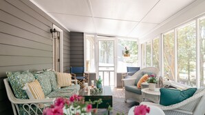A cozy room with a wicker sofa, a chair, and a coffee table. There is a door leading outside, and a window with a view of trees. - Peaceful Beach Retreat in Southern Shores.Beach Front Parking Passes included (Kitty Hawk)