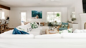 A spacious living room with a white sofa, a dining area with wicker chairs, and a large window providing natural light. - Peaceful Beach Retreat in Southern Shores.Beach Front Parking Passes included (Kitty Hawk)