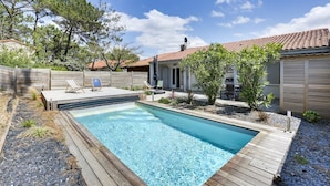 A rectangular swimming pool with a wooden deck, surrounded by a wooden fence and small plants.