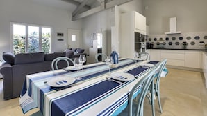 A modern kitchen with white cabinets, a dining area with striped tablecloths, and a gray sofa.