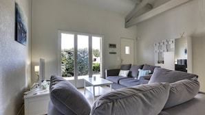 A modern living room with a grey sofa, a white coffee table, and a large sliding glass door leading to a balcony.
